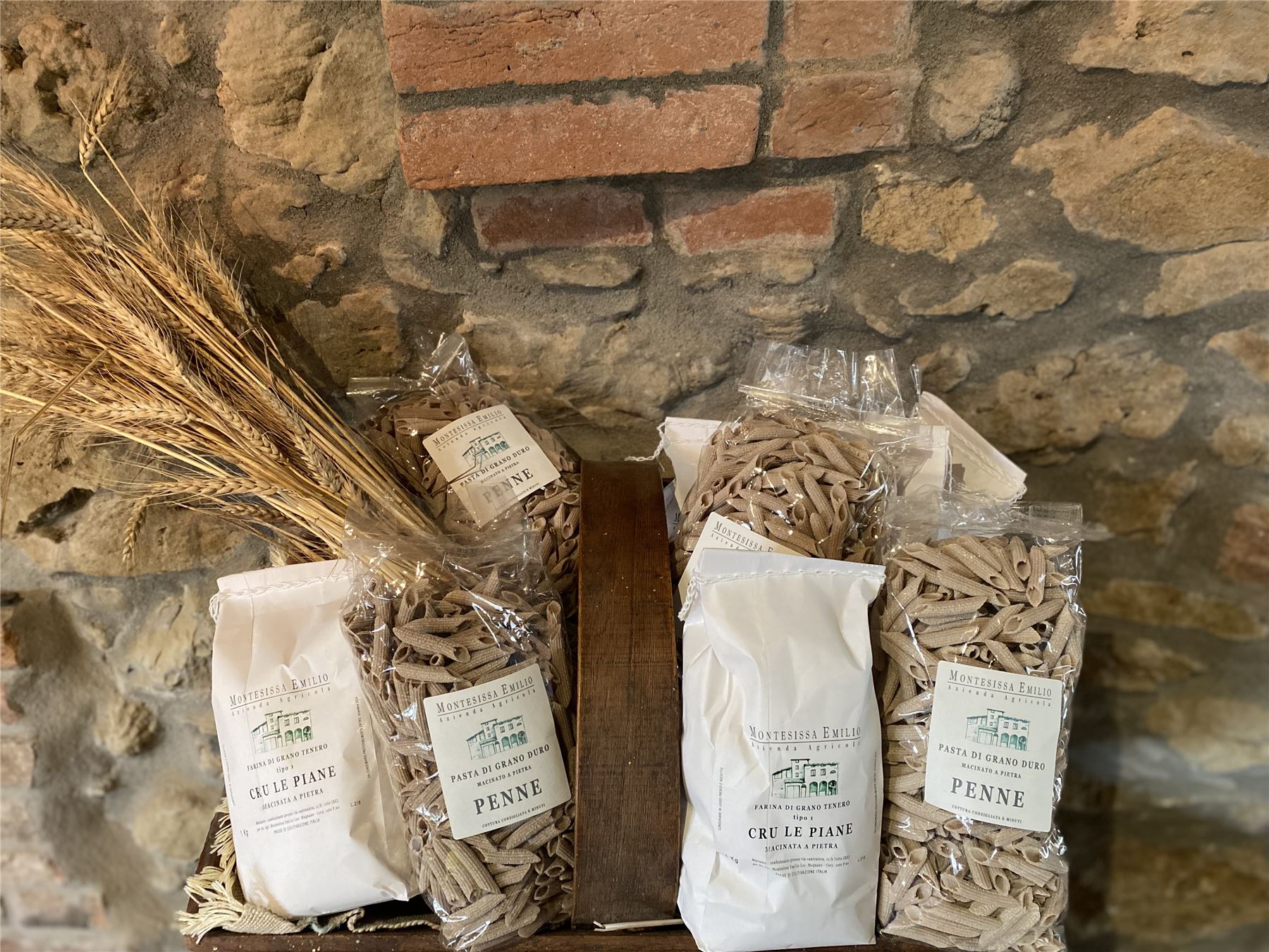 Sacchetti di farina e pasta Montesissa con spighe di grano su muro in pietra